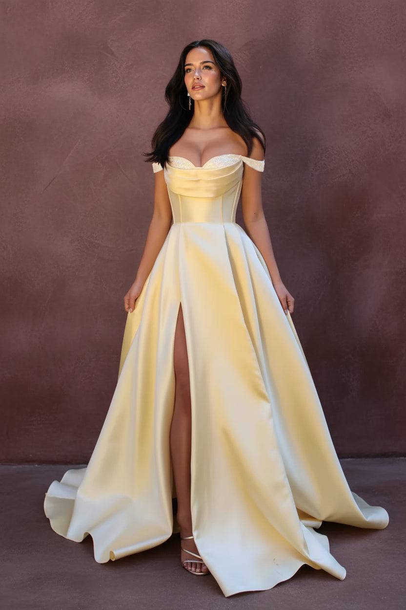 Woman in a yellow evening gown with a high slit standing outdoors among greenery.